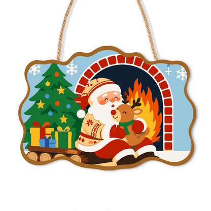 Santa's Fireside Reindeer Hug paint by numbers hanging sign – Santa hugging a young reindeer by a brick fireplace with a Christmas tree and presents, on a wooden sign with a rope hanger