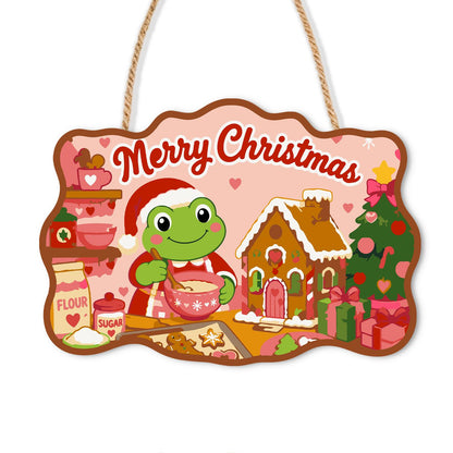 Mixing Bowl Frog Baker paint by numbers hanging sign – Frog in a Santa hat stirring a mixing bowl beside a gingerbread house, flour jar and Christmas tree on pink, on a wooden sign with a rope hanger