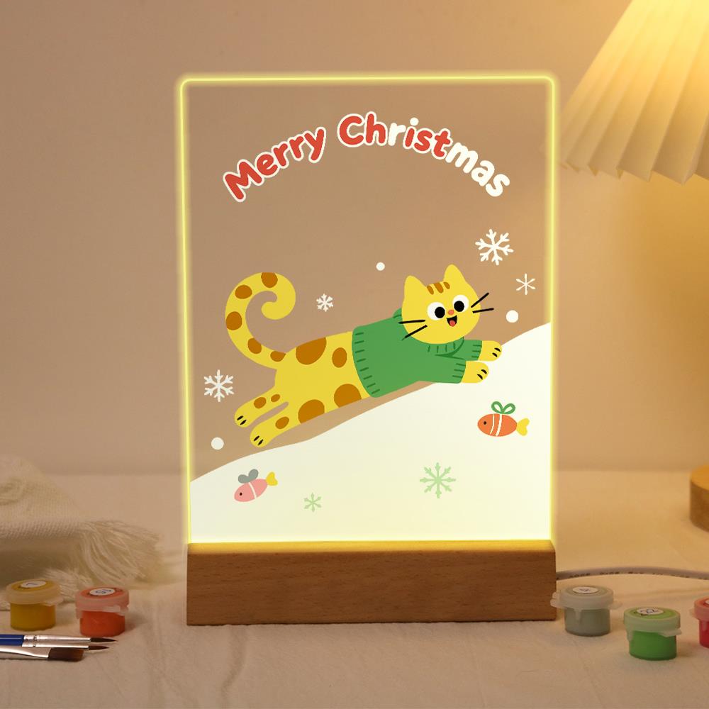 Sweater Cat's Snowy Leap paint by numbers light-up sign – Yellow spotted cat in a green sweater leaping over a snowy slope among snowflakes, gifts and fish, lit up on its wooden base