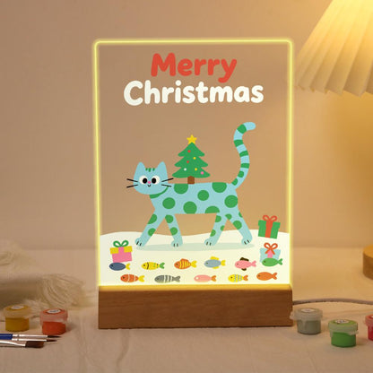 Spotted Cat Carrying a Tiny Tree paint by numbers light-up sign – Teal cat with green spots walking through snow with a small Christmas tree on its back, a gift and a row of fish below, lit up on its wooden base