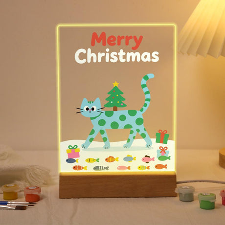 Spotted Cat Carrying a Tiny Tree paint by numbers light-up sign – Teal cat with green spots walking through snow with a small Christmas tree on its back, a gift and a row of fish below, lit up on its wooden base