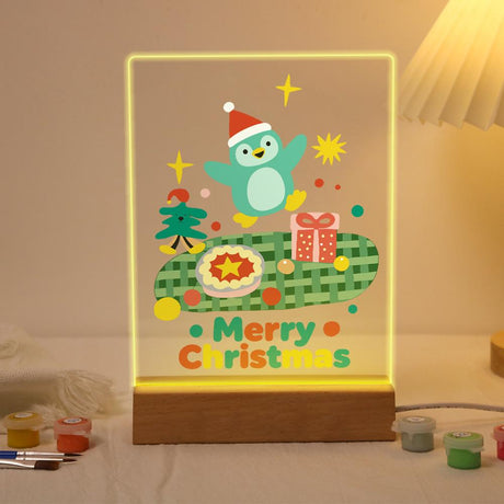 Penguin's Christmas Pie Picnic paint by numbers light-up sign – Teal penguin in a Santa hat leaping over a green checked blanket with a pie, a gift and a tiny tree, lit up on its wooden base