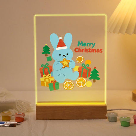 Blue Bunny with Gifts and Oranges paint by numbers light-up sign – Pale blue bunny in a Santa hat holding a star among gifts, orange slices and little trees, lit up on its wooden base