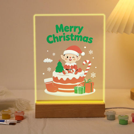 Elf Atop a Christmas Cake paint by numbers light-up sign – Little elf in a Santa hat sitting on a layered Christmas cake with gifts, a tiny tree and a candy cane, lit up on its wooden base