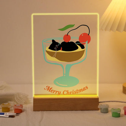 Black Cat in a Cherry Sundae paint by numbers light-up sign – Black cat lounging in a sundae glass of pudding topped with red cherries above Merry Christmas script, lit up on its wooden base