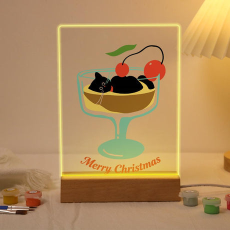 Black Cat in a Cherry Sundae paint by numbers light-up sign – Black cat lounging in a sundae glass of pudding topped with red cherries above Merry Christmas script, lit up on its wooden base