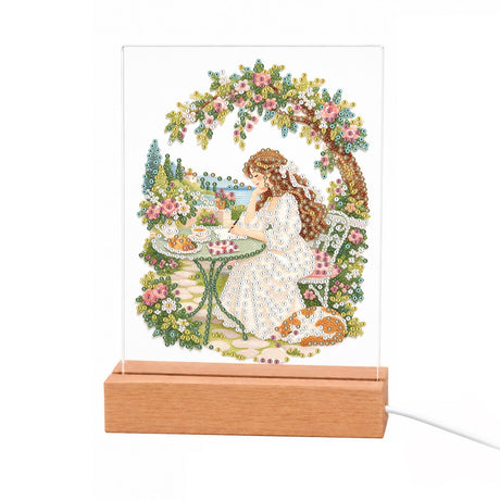 Teatime Under a Rose Arbor light-up pearl painting – Long-haired woman in white having tea at a garden table under a rose arch, a cat at her feet