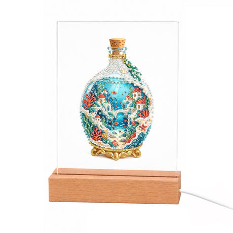 Seaside Village in a Corked Bottle light-up pearl painting – Round corked glass bottle on a gold stand holding white cliffside houses, blue sea and coral