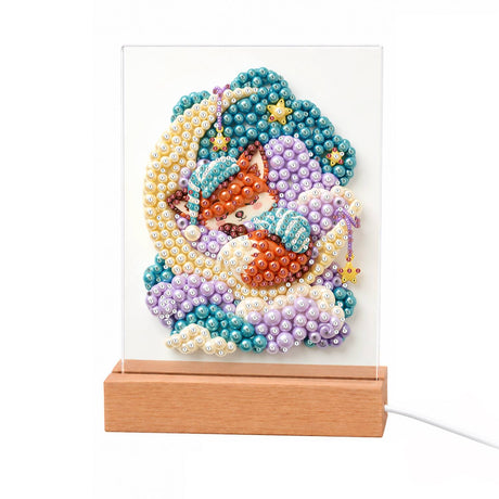 Nightcap Fox on a Crescent Moon light-up pearl painting – Orange fox in a teal nightcap asleep on a golden crescent moon among purple and teal clouds and stars