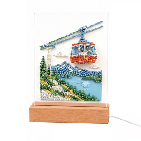 Red Gondola Over an Alpine Lake light-up pearl painting – Red cable car gondola over snowy blue mountains, a lake and green flowered hillsides