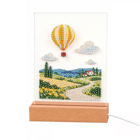 Striped Balloon Over Rolling Hills light-up pearl painting – Yellow-and-white striped hot-air balloon above rolling green fields, a winding path and a red-roofed farmhouse