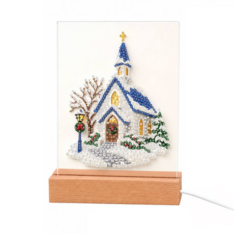 Blue-Roofed Chapel in the Snow light-up pearl painting – White chapel with a blue roof and steeple, gold cross, wreathed door and bare winter tree in snow