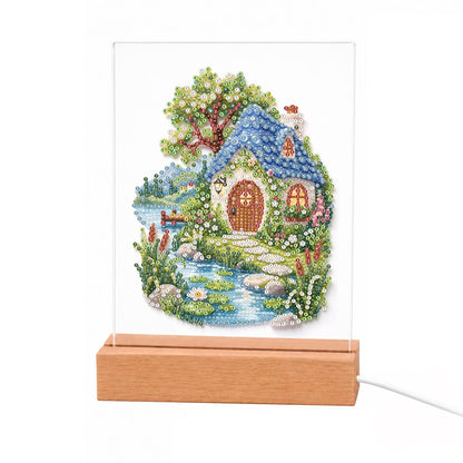 Blue-Roofed Cottage by a Stream light-up pearl painting – Cottage with a blue rounded roof and arched wooden door beside a stream, a leafy tree and wildflowers