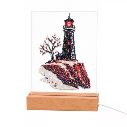 Black Lighthouse on Red Cliffs light-up pearl painting – Black lighthouse with a red lantern room on dark red cliffs beside a bare tree with pink blossoms
