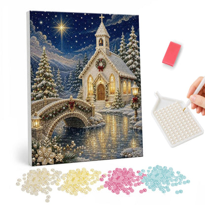 Little White Chapel at Christmas pearl painting – White chapel with a wreath and lit windows beside an arched stone bridge over a river on a starry snowy night