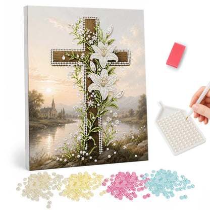 Lily-Draped Cross by the Lake pearl painting – Wooden cross wrapped in white lilies beside a calm lake with a church in the distance at golden hour