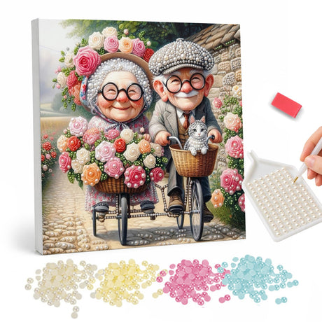 Grandparents' Flower Basket Ride pearl painting – Smiling elderly couple in glasses riding bicycles with baskets of roses and a cat on a cobbled lane