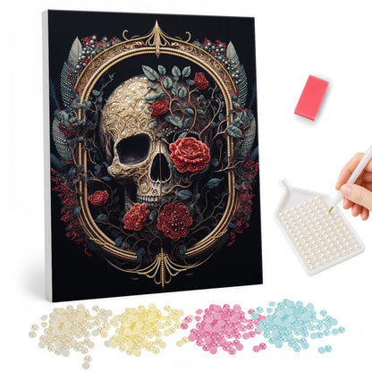 Skull in a Gilded Rose Frame pearl painting – Cream skull wreathed in red roses and dark leaves inside an ornate gold oval frame on black
