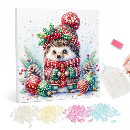Hedgehog in a Holly Bobble Hat pearl painting – Hedgehog in a red bobble hat with holly and a red knit sweater among baubles and pine cones