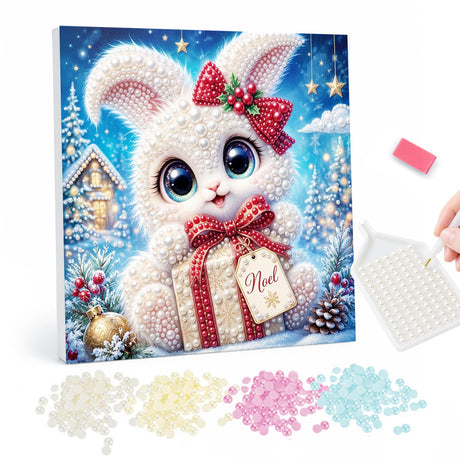 Snow Bunny with a Noel Gift pearl painting – Fluffy white bunny with a red bow on its ear holding a gift tagged Noel in a snowy village