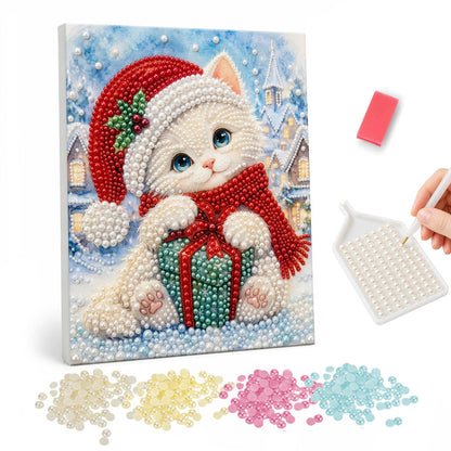White Kitten Hugging a Gift pearl painting – White kitten in a Santa hat and red scarf hugging a teal gift in a snowy village