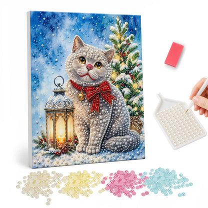 Grey Cat with a Plaid Bow pearl painting – Grey cat wearing a red plaid bow sitting in snow between a lantern and a lit Christmas tree