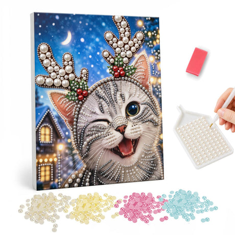 Winking Kitten in Antler Headband pearl painting – Winking grey tabby kitten wearing a white antler headband in a snowy village under a crescent moon