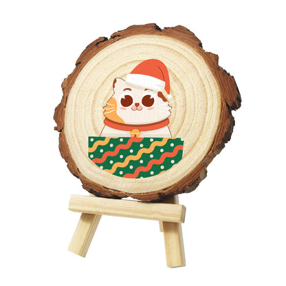 Bell-Collar Cat in a Santa Hat paint by numbers wood slice – Ginger-patched cat in a Santa hat and bell collar peeking over a green box with wavy red stripes, painted on a pine slice on a small easel