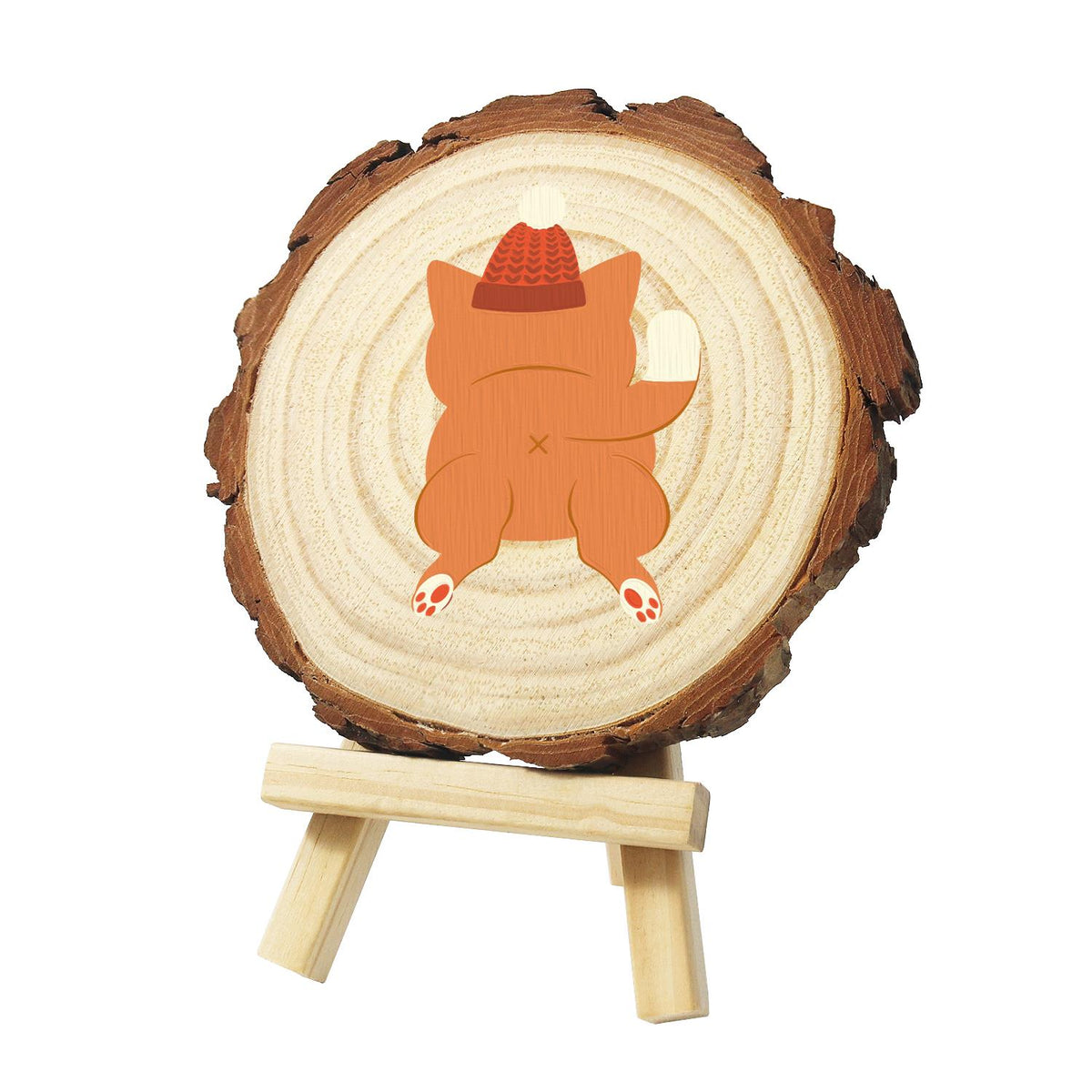 Ginger Cat in a Bobble Hat paint by numbers wood slice – Orange cat seen from behind in a red knit bobble hat, one paw raised and paw pads showing, painted on a pine slice on a small easel