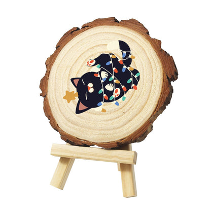 Black Cat Tangled in Lights paint by numbers wood slice – Black cat rolling on its back wrapped in colourful string lights, with a small gold star, painted on a pine slice on a small easel